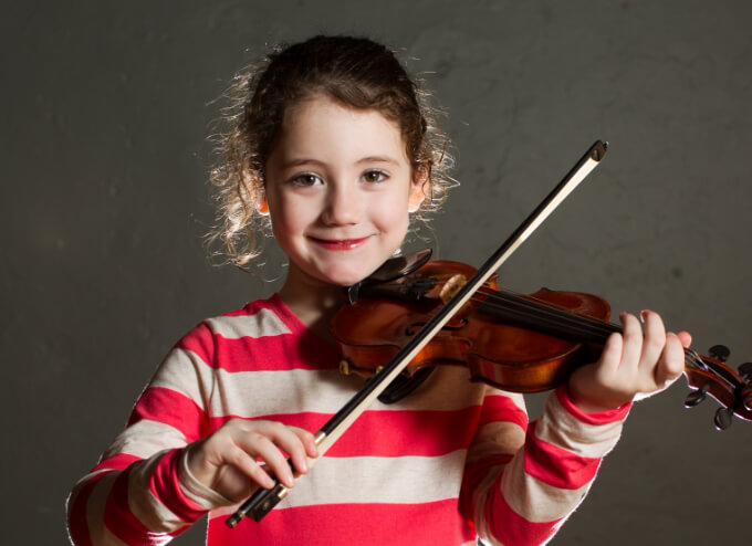 Young girl in striped shirt playing violin, smiling.