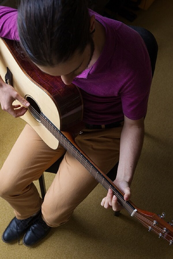 Man in purple shirt and tan pants playing an acoustic guitar