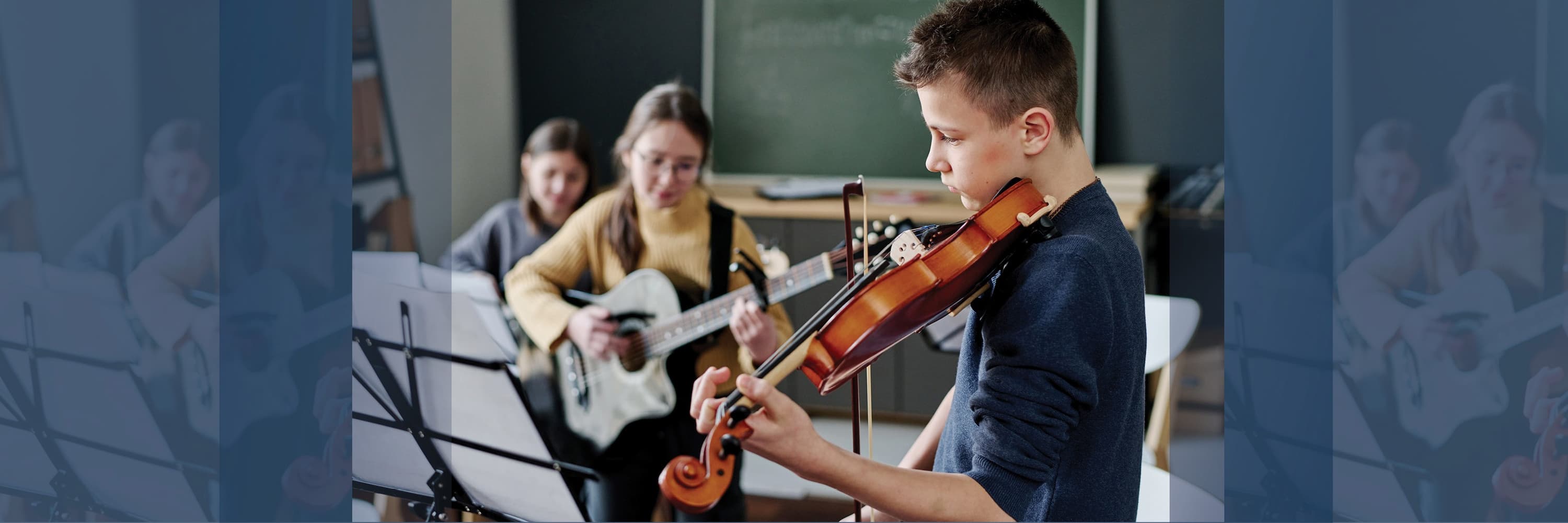 Boy playing violin with two girls playing guitar in a music classroom