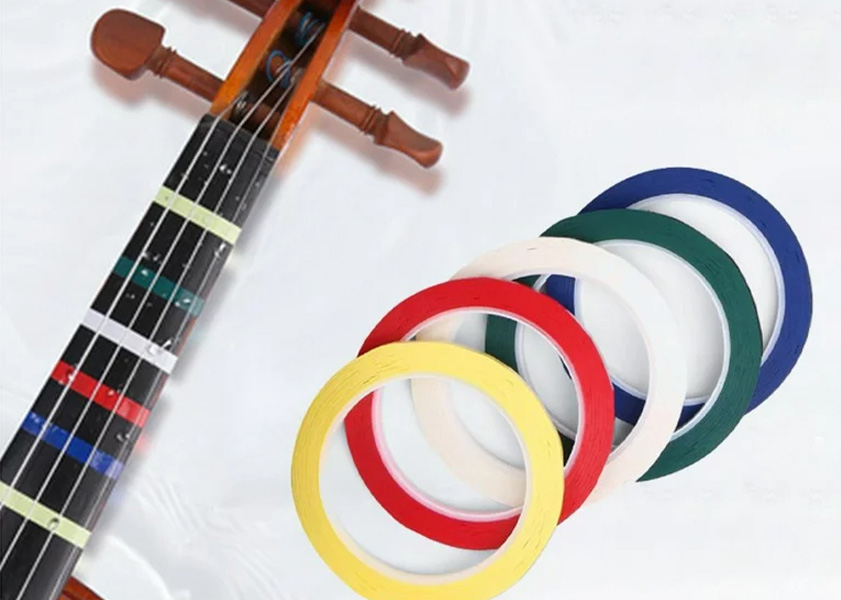 Violin fingerboard with colored tapes and rolls of tape beside it.