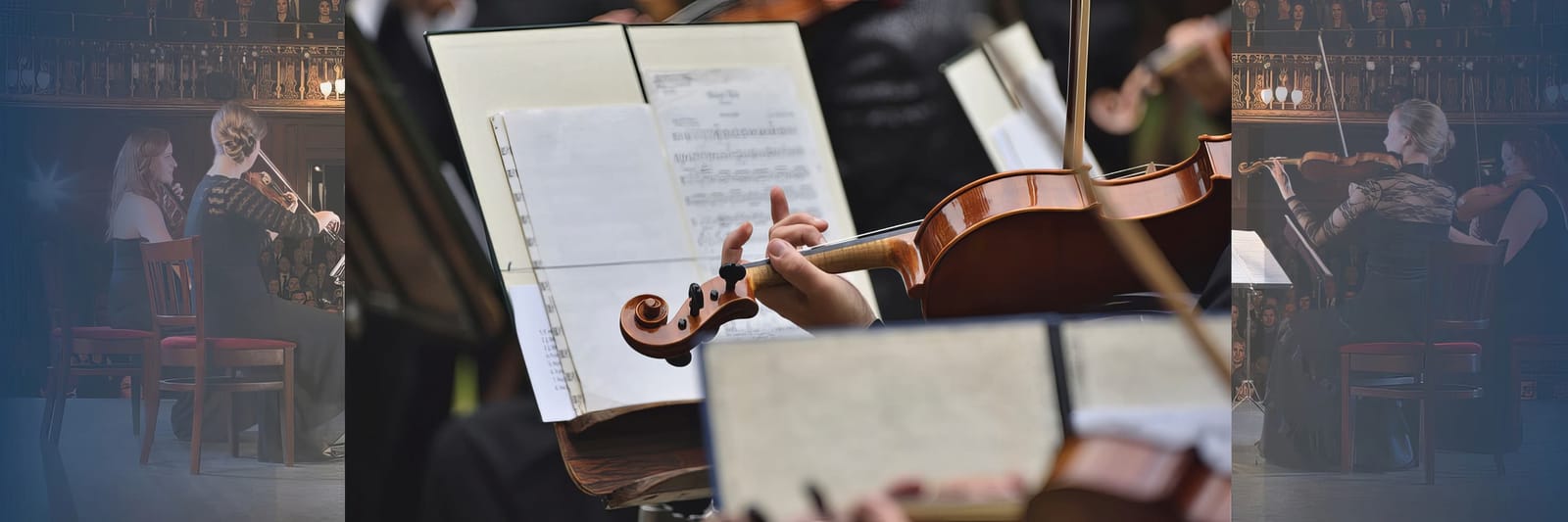 Close-up of violinist's hand playing near sheet music, with musicians performing in the background.