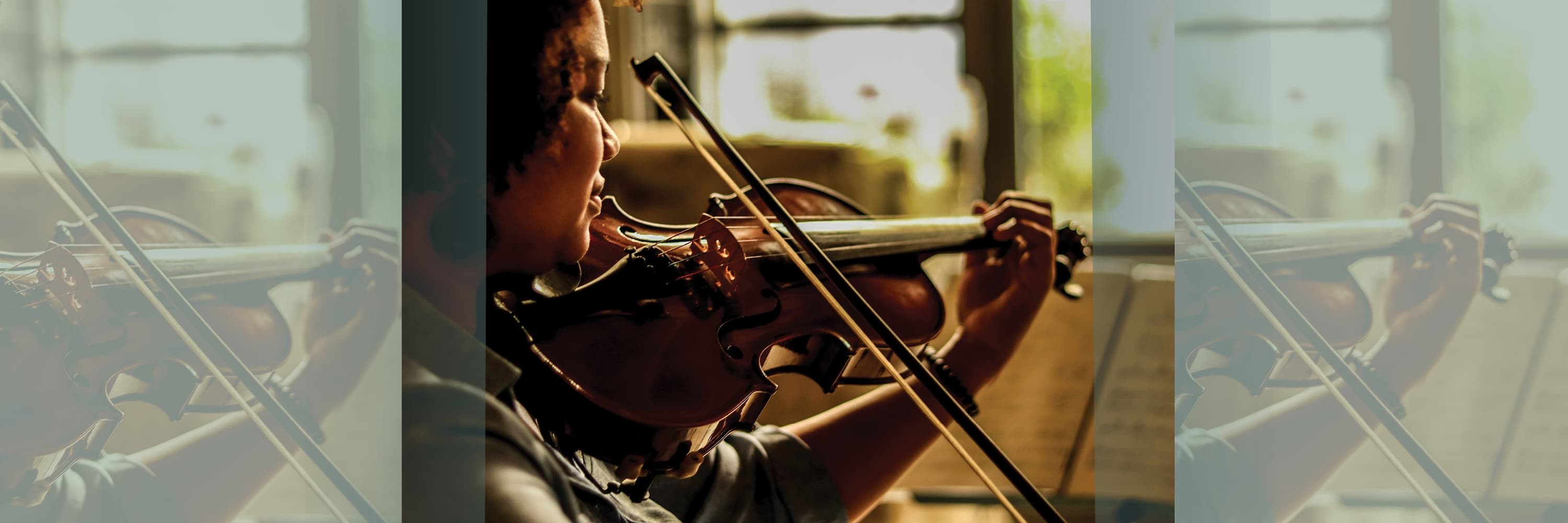 A young violinist playing near a window in warm natural light