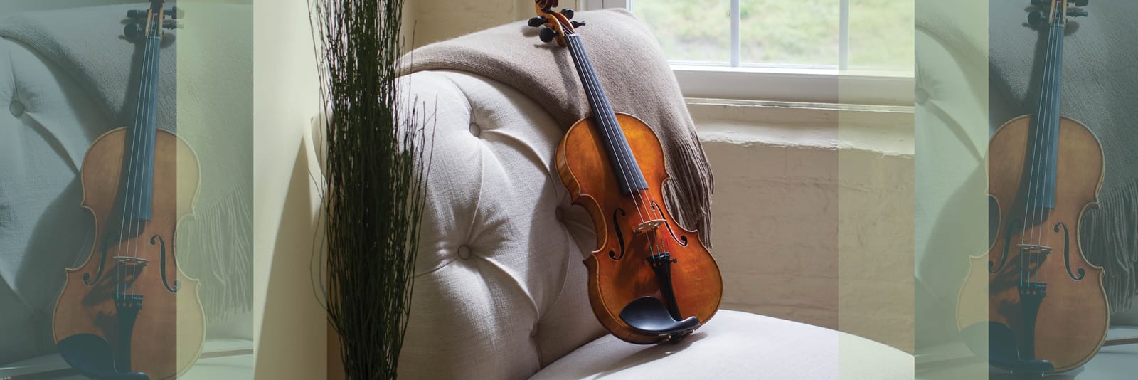 A violin resting against an upholstered armchair in a home living room, near a sunlit window