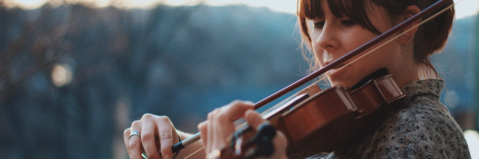 Woman playing a violin outdoors with a blurred background.