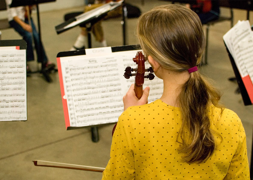 Young musician in a yellow dotted shirt practicing violin in front of a music stand with sheet music