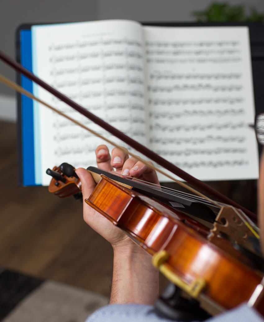 Person playing a violin with sheet music in the background.