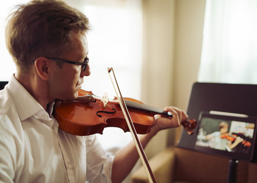 Man in glasses practicing violin while looking at digital music sheet on tablet