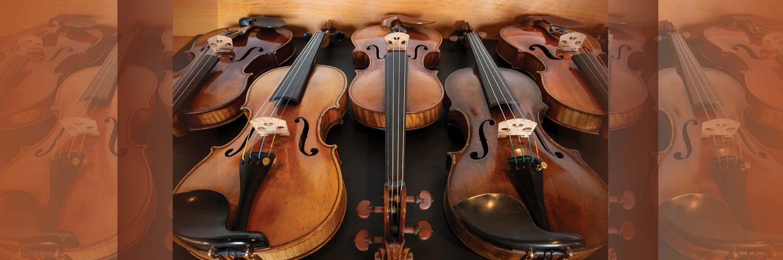 Five wooden violins arranged side by side on a dark surface