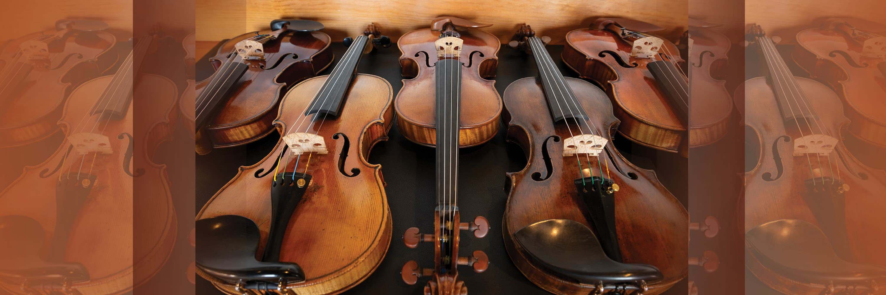 Five wooden violins arranged side by side on a dark surface