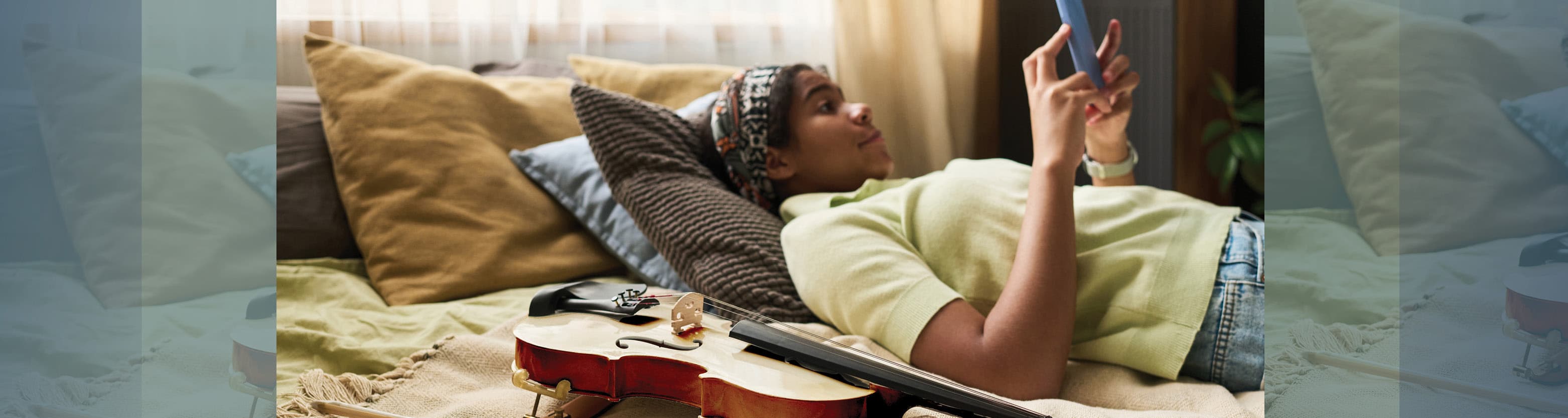 Person lying on a bed using a smartphone with a violin and bow resting nearby on the blanket