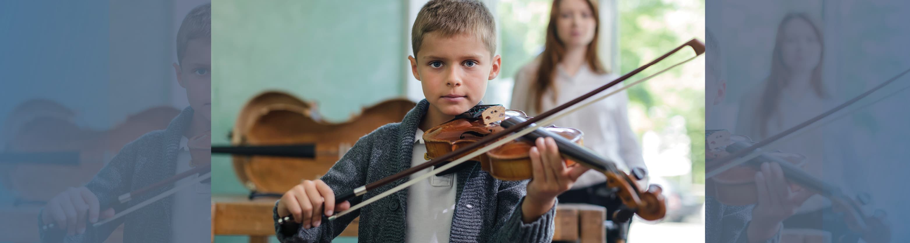Young boy playing violin in a classroom with a woman standing in the background