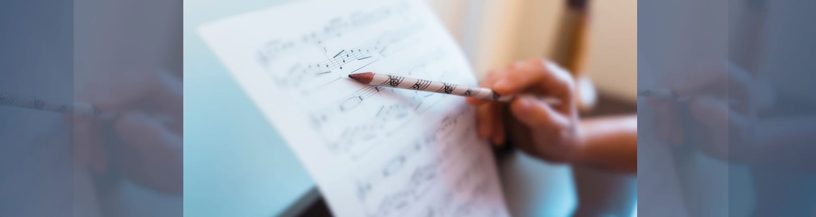 Hand holding a pencil pointing at sheet music on a stand, with musical notes visible