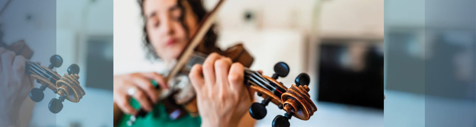 Close-up of a person playing the violin with focus on the instrument's scroll and tuning pegs
