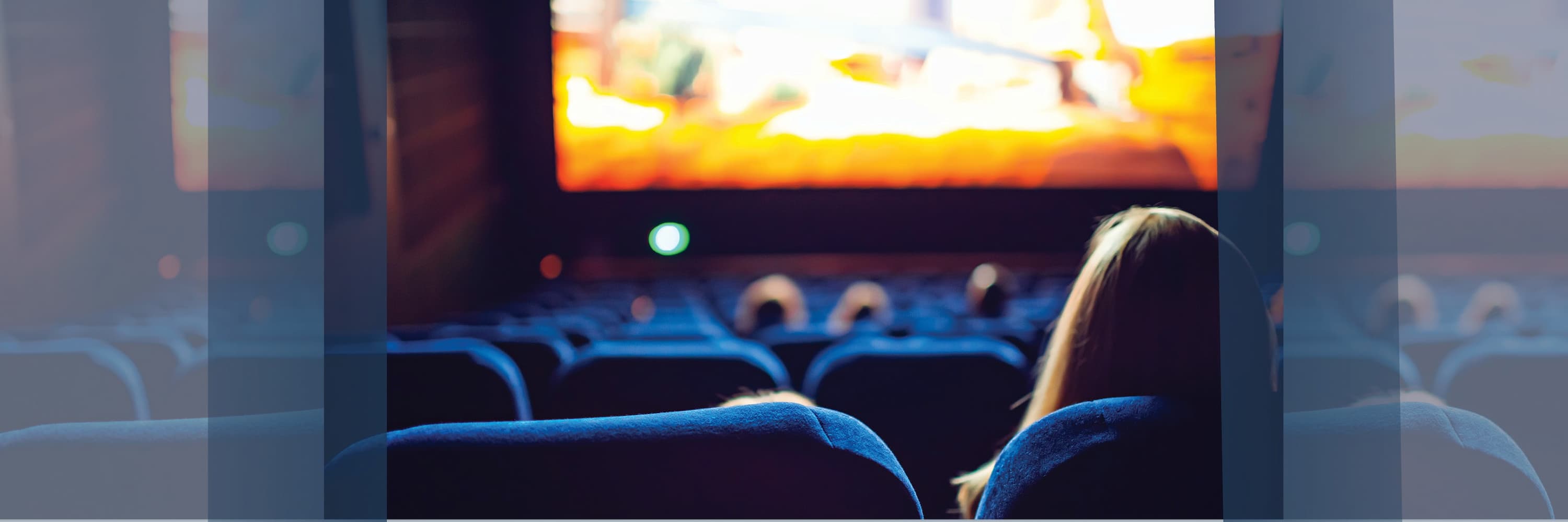 People seated in a dark movie theater watching a brightly lit screen ahead