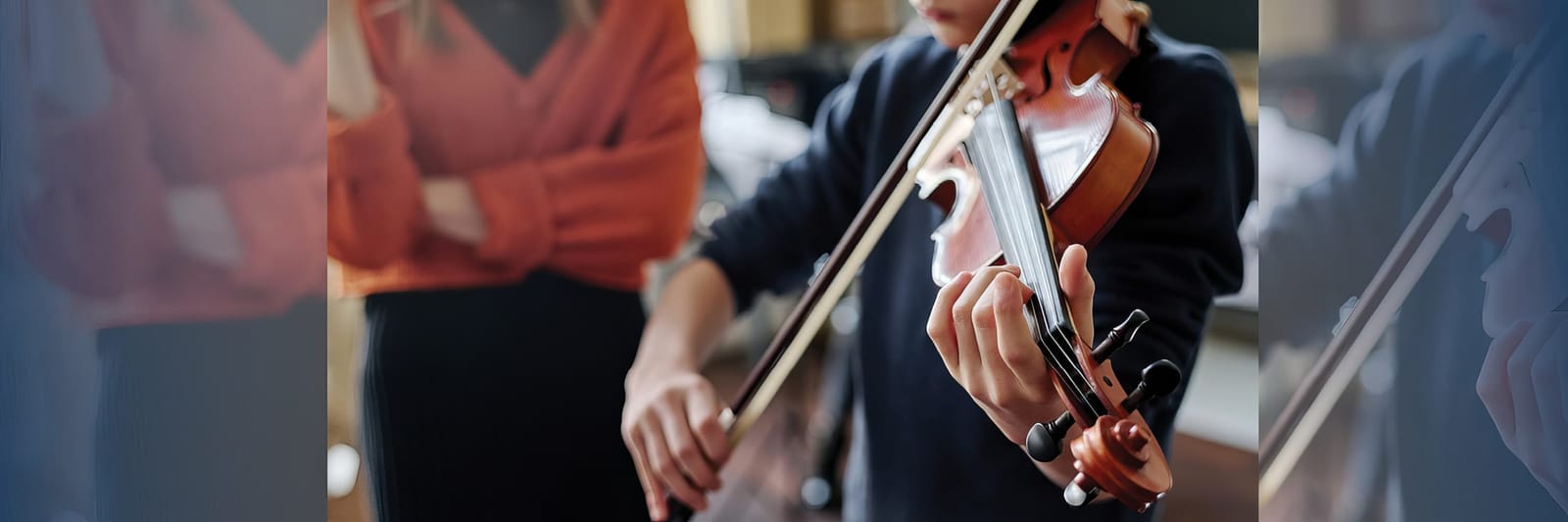Student playing violin while instructor watches closely in the background