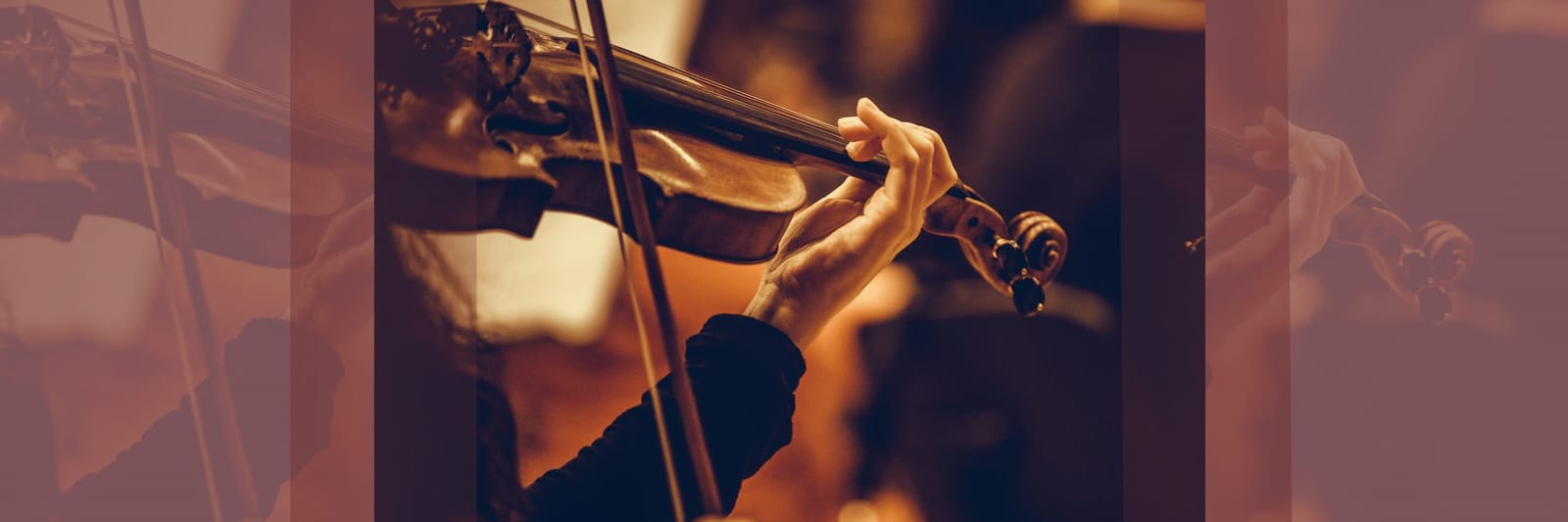 Hand playing a violin with a bow in warm, low-light setting