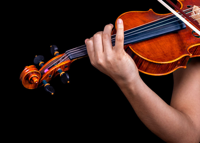 Close-up of a hand positioning fingers on the fingerboard of a violin against a black background