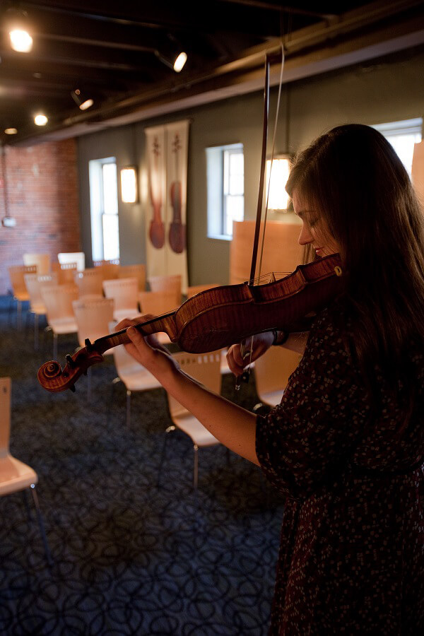 Woman playing a violin in a dimly lit room with empty chairs