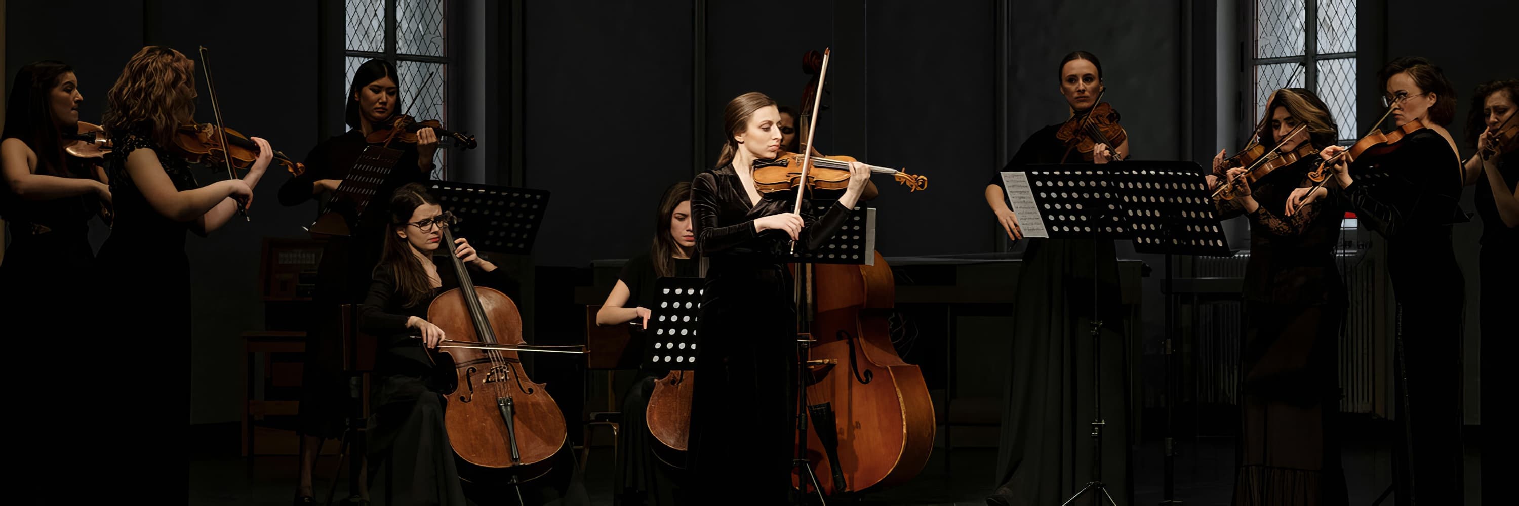 Women in black dresses performing classical music in an orchestra with string instruments