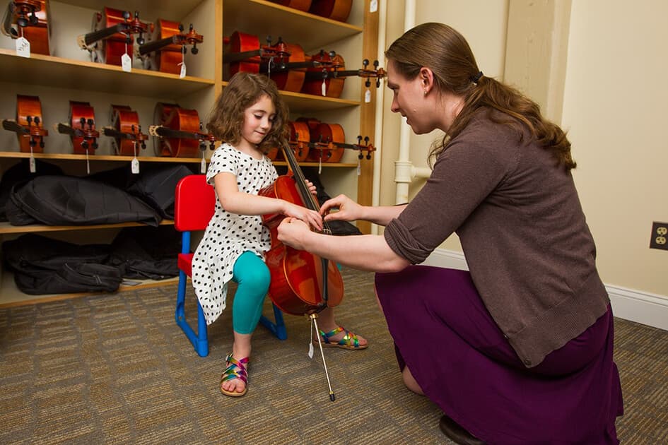 Woman kneeling to help girl with cello technique