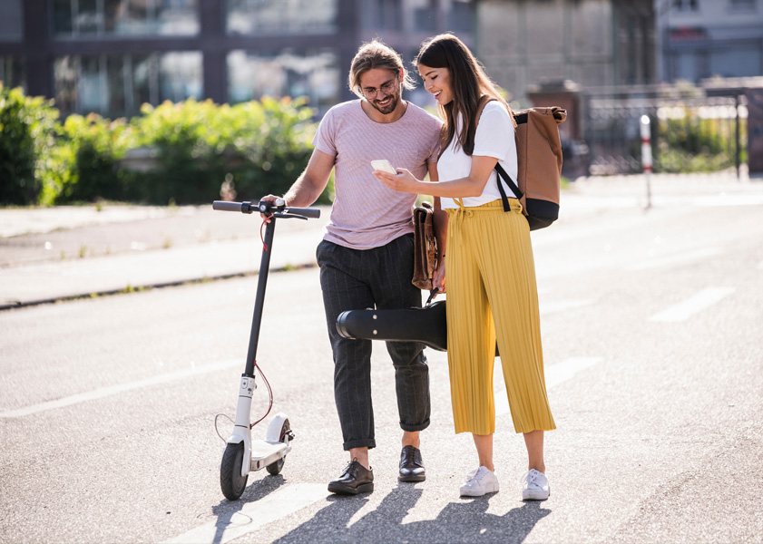 Man with a scooter and woman holding a violin case, both looking at a phone