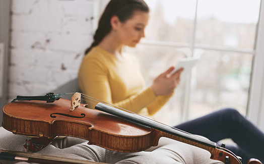 Woman reads a book in the background with violin in the foreground