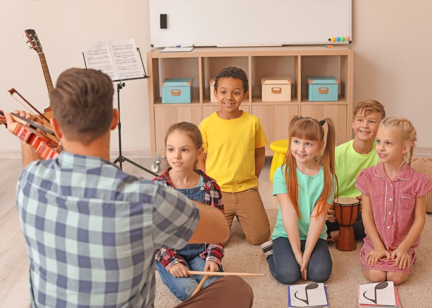 Teacher playing violin for a group of attentive children in a classroom
