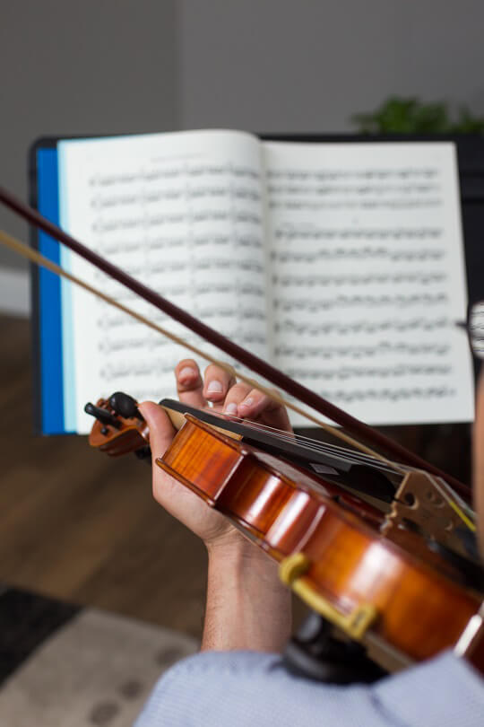 Person playing a violin with sheet music in the background