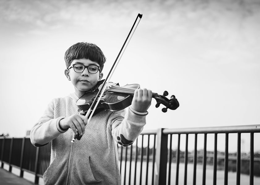 Young boy playing violin on a bridge in black and white
