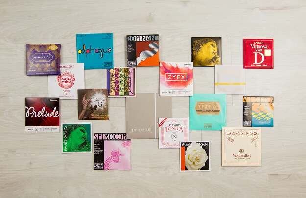Collection of various violin string packages arranged on a light wooden surface